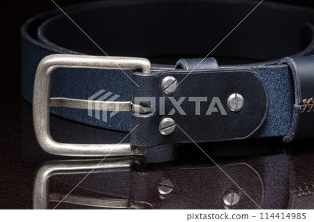 Leather belt with a metal buckle close-up on a dark background. 114414985