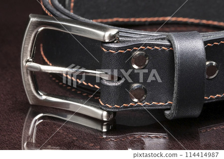 Black leather belt with a metal buckle on a dark background close-up. 114414987
