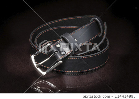 Black leather belt with a metal buckle on a dark background close-up. Black leather belt with a metal buckle on a dark background close-up. 114414993