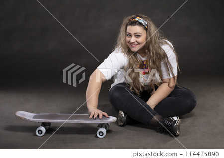 Beautiful plump woman with a skateboard on a gray background. Beautiful plump woman with a skateboard on a gray background. 114415090