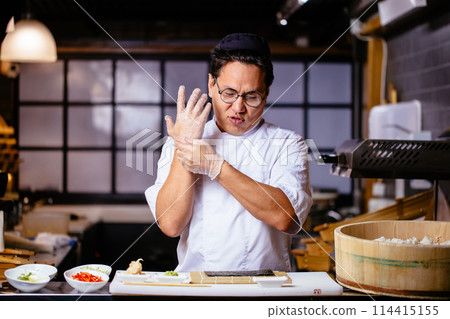 young handsome Asian chef is putting on gloves before cooking rolles young handsome Asian chef is putting on gloves before cooking rolles 114415155