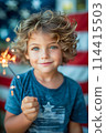 Portrait of a small blond boy against the background of the national flag of America and with a sparkler in his hands. The concept of celebrating Independence Day in America on July 4th. 114415503