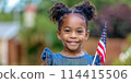 A charming dark-skinned little girl happily holds an American flag in her hands. This image reflects the idea of celebrating the Independence Day of the United States, which is celebrated on July 4 114415506