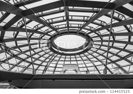 Inside view of the Reichstag glass dome in Berlin showing the top part with circular bench under the glass rooftop and steel framework. Berlin, Germany. Black and white image. 114415525