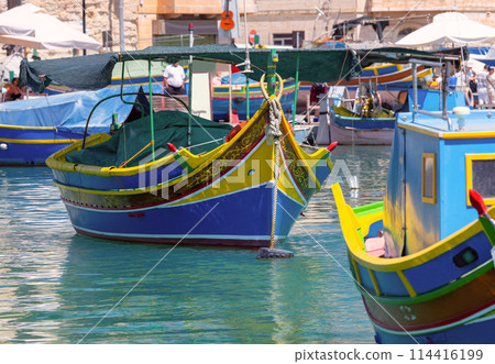 Multi-colored fishing boats luzzi with eyes in the harbor of the village Marsaxlokk on the island Malta. Multi-colored fishing boats luzzi with eyes in the harbor of the village Marsaxlokk on the island Malta. 114416199