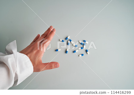 Hand reaches out to a white and blue pill on a blue background. 114416299