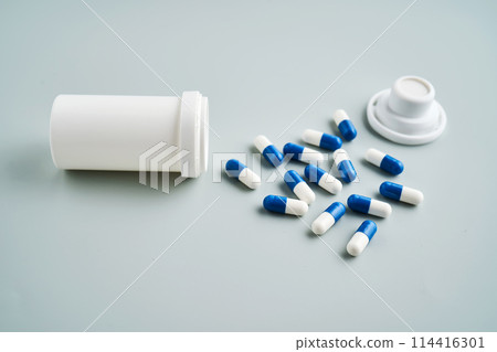 Blue and white capsules spilled out of a medicine jar on a blue background. 114416301