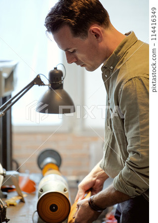 talented male master grinds and polishes the edges of the leather 114416349