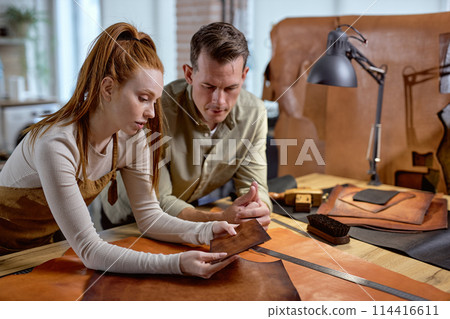 young ginger girl checking a quality of a leather piece. 114416611