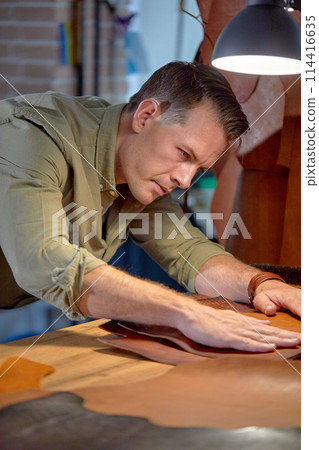 handsome brown-haired guy prepares leather for sewing handsome brown-haired guy prepares leather for sewing 114416635
