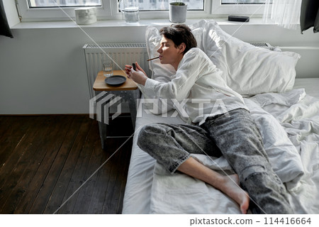 drunk man lighting cigarette in the bedroom 114416664