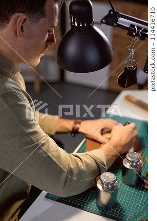 young artisan punctures holes into leather young artisan punctures holes into leather 114416710