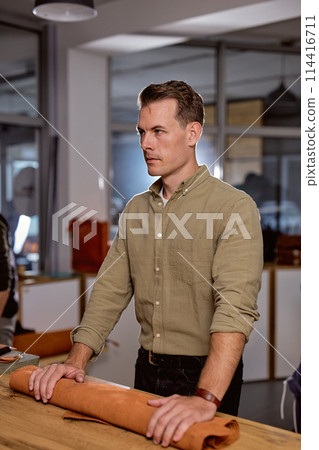 serious skilled tailor holds rollof natural brown leather 114416711