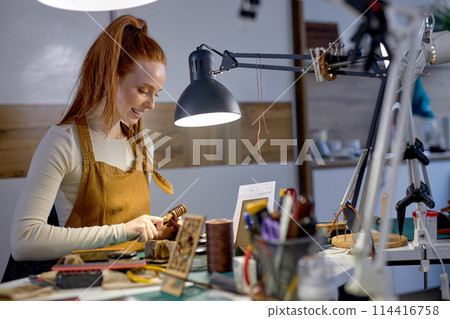 cheerul pretty cratswoman burnishes the edge of wallet before painting 114416758