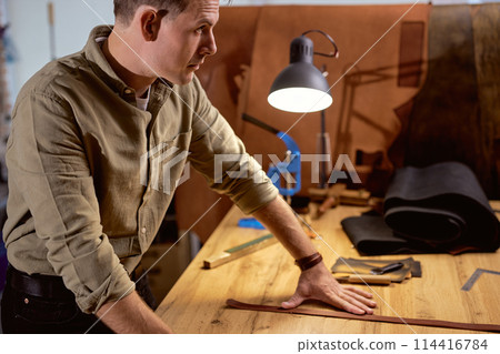 pensive thoughtful craftsman working with piece of leather in workshop 114416784