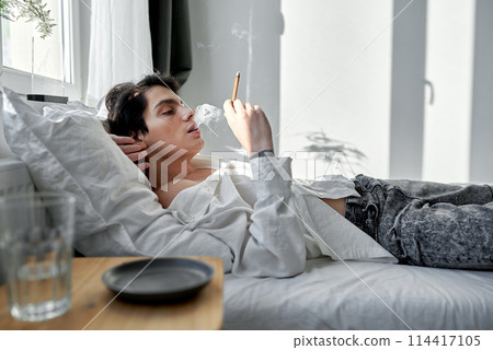 handsome man smoking blunt with medical cannabis in apartment handsome man smoking blunt with medical cannabis in apartment 114417105