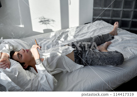 man smoking weed lyinng in bedroom. full length side view shot 114417319