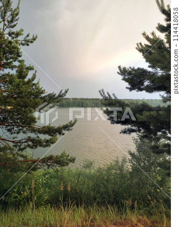 Vacation in nature with a natural landscape: coast, cliff, lake shore in a forest with pines and fir trees, waves on the water, sky after rain with clouds and clouds with natural light on a summer Vacation in nature with a natural landscape: coast, cliff, lake shore in a forest with pines and fir trees, waves on the water, sky after rain with clouds and clouds with natural light on a summer 114418058