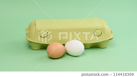 Two chicken eggs in a paper box on a green background Two chicken eggs in a paper box on a green background 114418309
