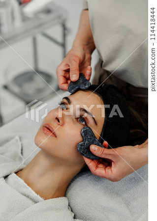 Woman receiving facial massage in beauty salon. Woman receiving facial massage in beauty salon. 114418444