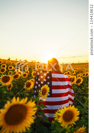 Beautiful girl with the American flag in a sunflower field. 4th of July. Fourth of July. Freedom. 114418612