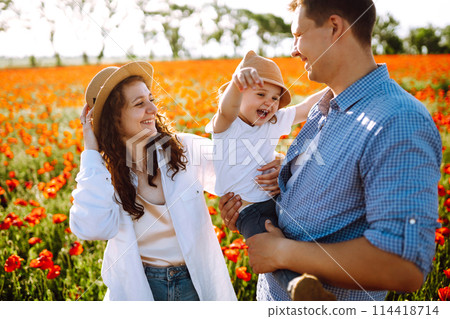 Family with a child walking on a poppy field. Mother, father, little daughter having fun on the poppy field. Family with a child walking on a poppy field. Mother, father, little daughter having fun on the poppy field. 114418714