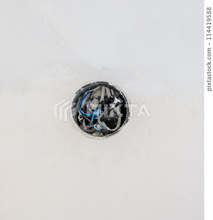 An electrical junction box on a white wall. The electrical wires start from the wall. The concept of laying an electrical cable. 114419588