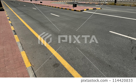 An empty curving auto road with distinct yellow restriction lines, white lane markings and a sidewalk edge 114420833
