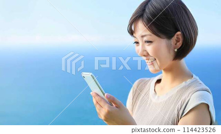 A woman using a smartphone with the sea in the background 114423526
