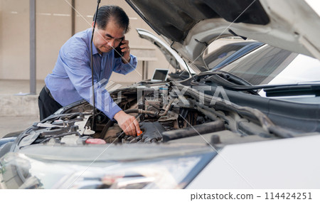 Senior man work on a vehicle, engaged in a car repair or inspection while using a mobile phone, possibly seeking advice or discussing the issue with someone, focus on the engine compartment of the car Senior man work on a vehicle, engaged in a car repair or inspection while using a mobile phone, possibly seeking advice or discussing the issue with someone, focus on the engine compartment of the car 114424251