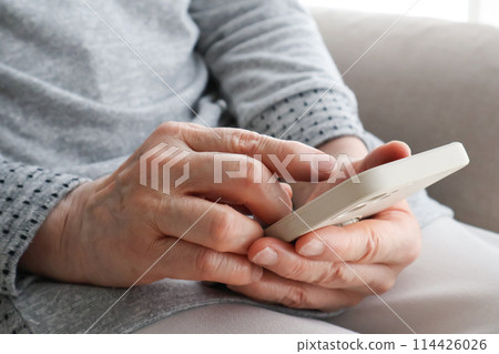 Senior woman's hand operating a smartphone Senior woman's hand operating a smartphone 114426026