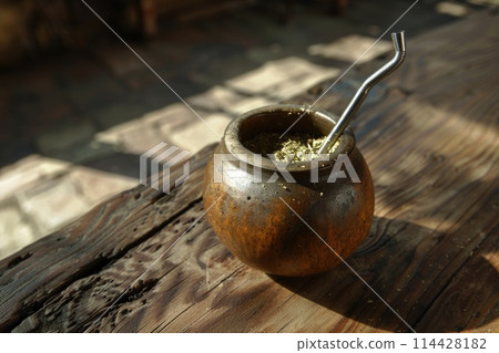 Traditional Argentine Mate displayed on a rustic wooden surface with a bombilla in a cozy setting 114428182