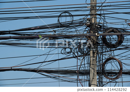 Electric post and line are on blue background.Electric post is covered by busy electric line. 114428292