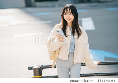A woman thinking with her smartphone on the roadside 114429063