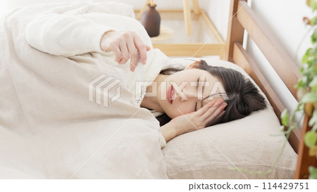 A woman measuring her temperature with a thermometer while lying down A woman measuring her temperature with a thermometer while lying down 114429751