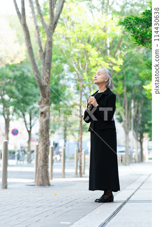 Senior woman in mourning clothes looking up at fresh greenery Senior woman in mourning clothes looking up at fresh greenery 114430638
