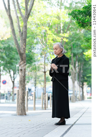 Senior woman in mourning clothes looking up at fresh greenery 114430641