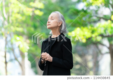 Senior woman in mourning clothes looking up at fresh greenery 114430645