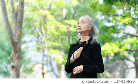Senior woman in mourning clothes looking up at fresh greenery 114430650