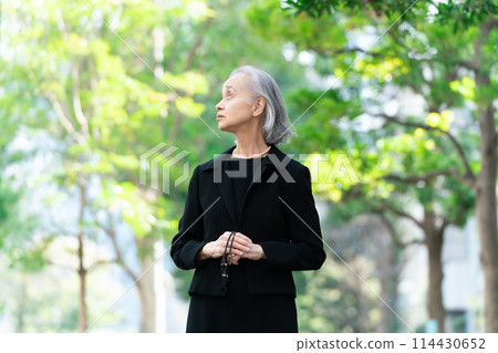 Senior woman in mourning clothes looking up at fresh greenery 114430652