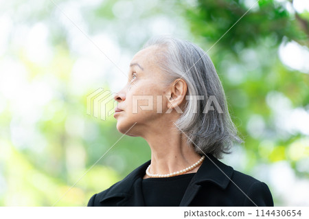 穿著喪服的老婦人抬頭看著新鮮的綠色植物 114430654