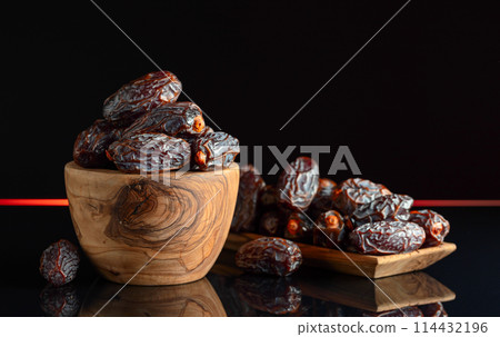 Dates in wooden dish on a black background. 114432196