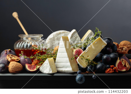Camembert cheese with fruits and honey on a black background. Camembert cheese with fruits and honey on a black background. 114432203