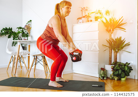 middle-aged woman does yoga in bright spacious room with house plants middle-aged woman does yoga in bright spacious room with house plants 114432575