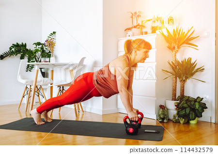 middle-aged woman does yoga in bright spacious room with house plants 114432579