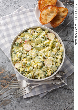 Homemade salad of eggs, radishes, green onions and cucumber dressed with mayonnaise close-up in a bowl. Vertical top view 114433037