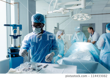 african man in mask and cup taking surgical instruments 114433082
