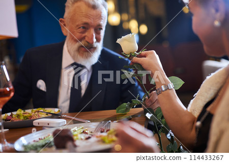 Loving man presenting white flower to his woman. Couple celebrating anniversary in restaurant 114433267