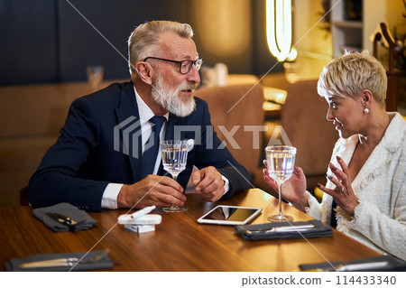 Attractive senior couple sitting in restaurant table and speaking Attractive senior couple sitting in restaurant table and speaking 114433340