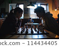 Two young individuals deeply engrossed in a strategic game of chess, competition under soft lighting 114434405